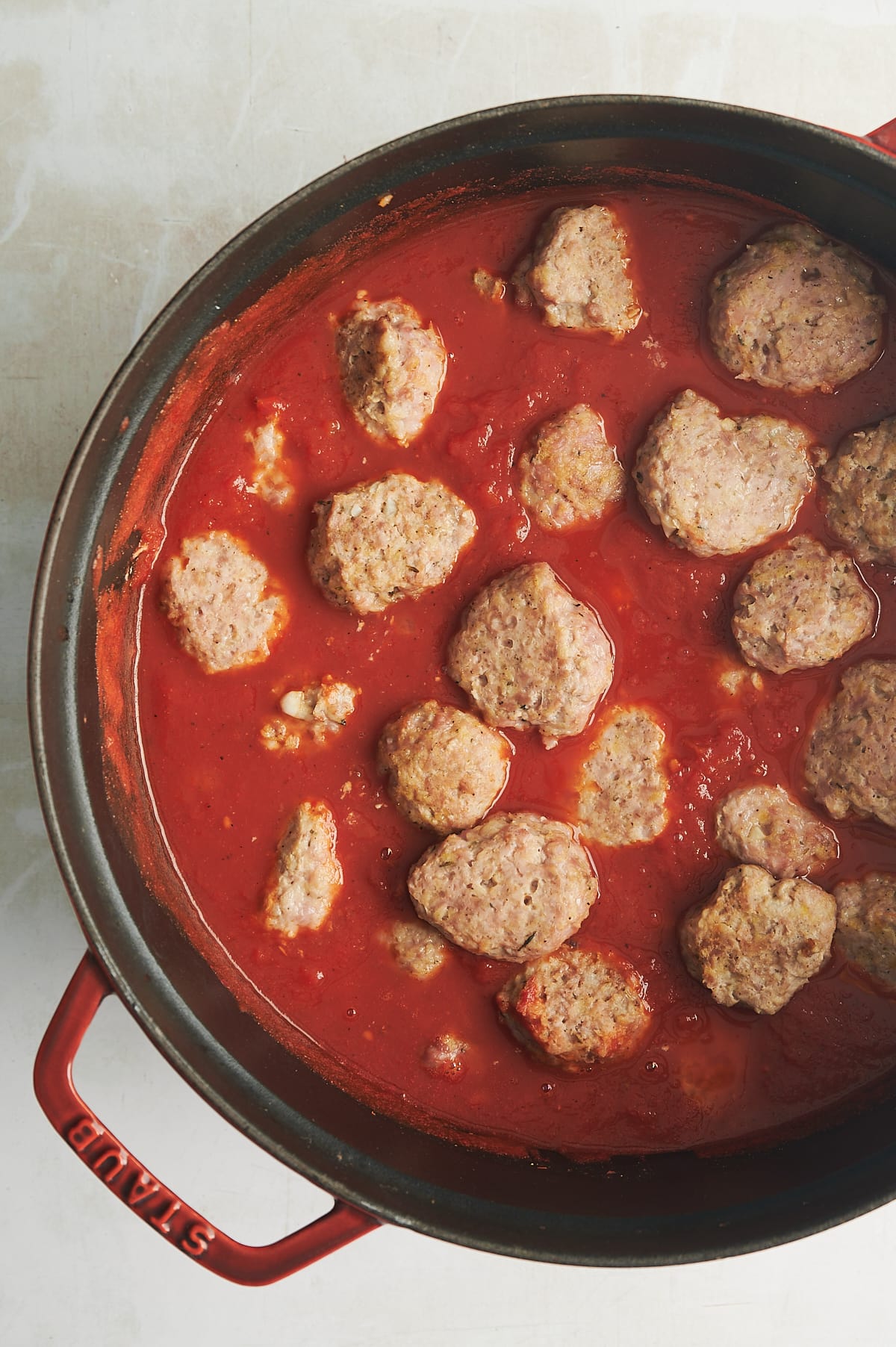 black lined Dutch oven with tomato sauce filled with chicken meatballs.