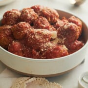 Finished bowl of chicken meatballs and parmesan with Italian red sauce with lacy napkin and spoon.