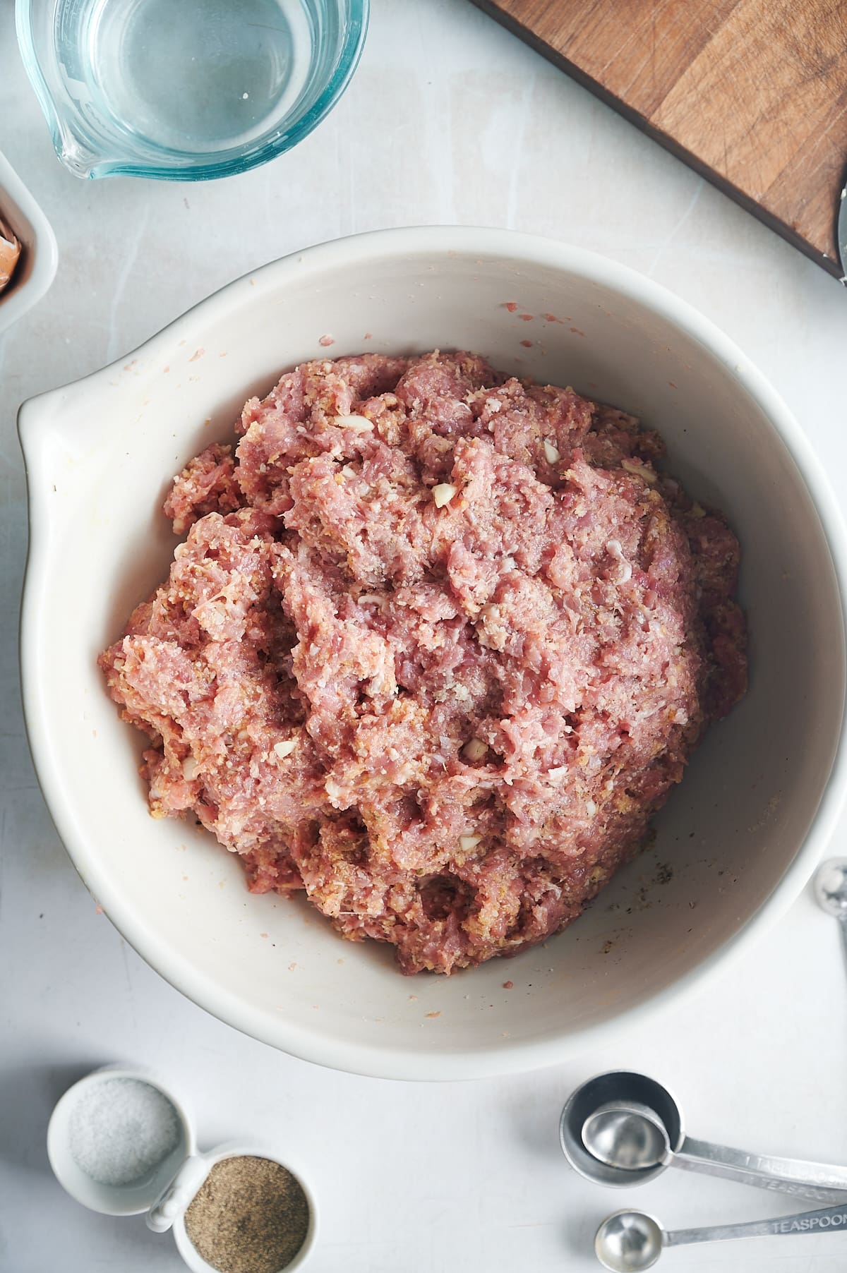 white bowl of chicken meatball mix with bowls of salt, pepper and measuring spoons.