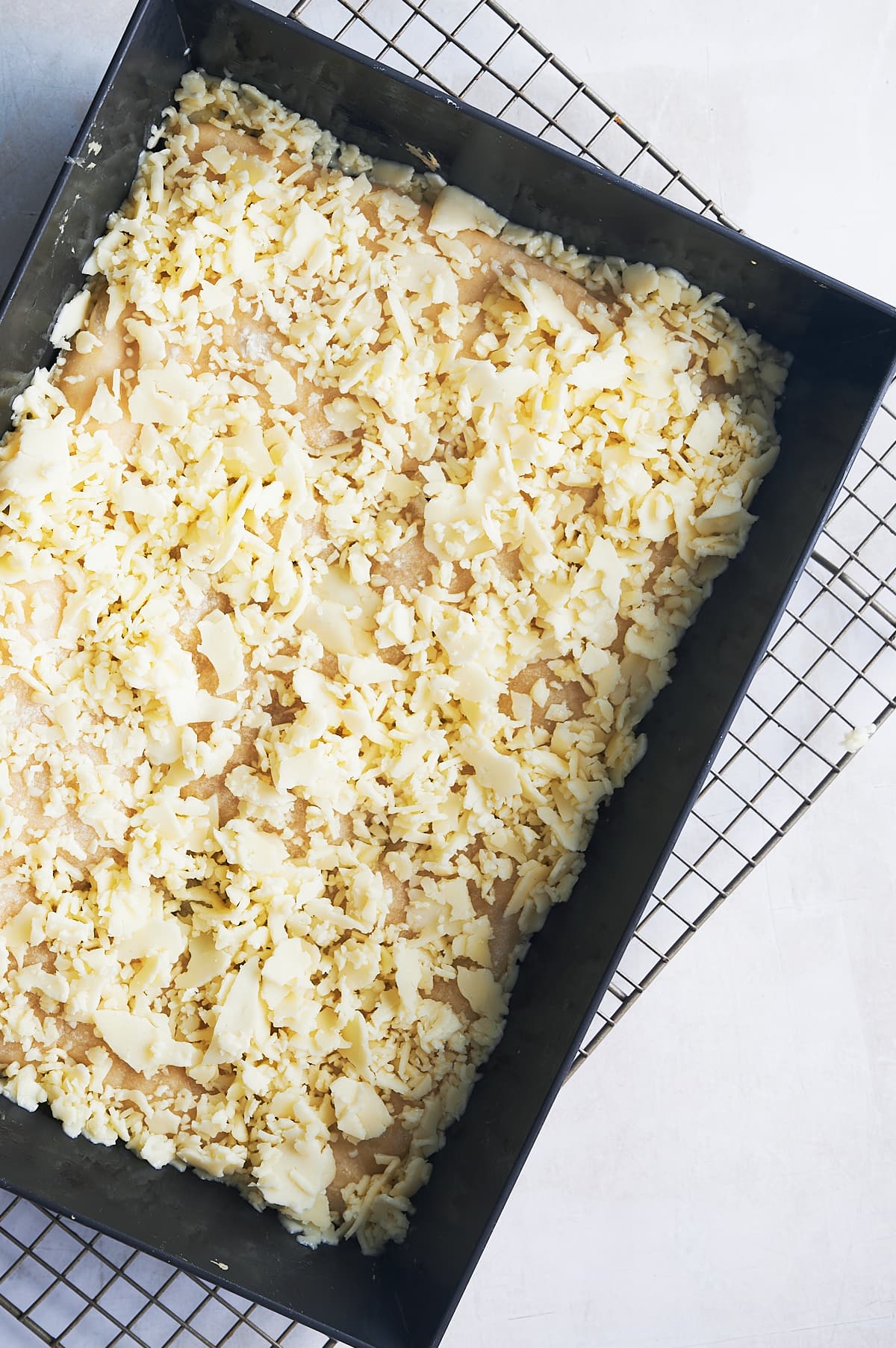 Grated brick cheese sprinkled on Detroit pizza in pan.