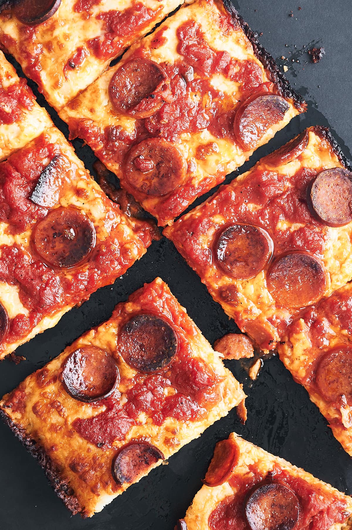 Sliced Detroit pan pepperoni pizza on black pizza peel.
