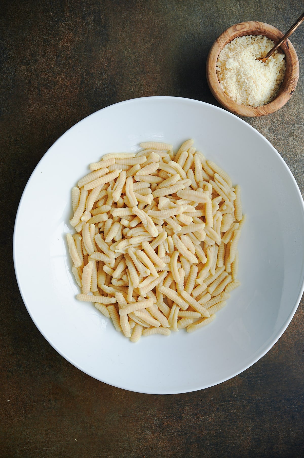 white bowl of cooked ricotta cavatelli with wooden bowl of parmesan cheese.