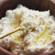 Close up of a wooden bowl of homemade ricotta cheese drizzled with olive oil and a brass spoon in it
