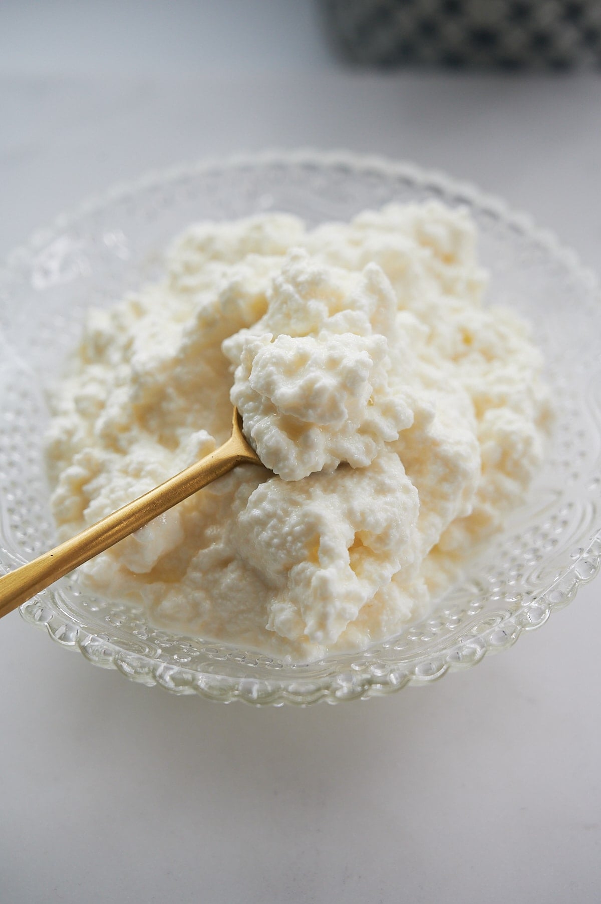 clear embossed bowl of homemade ricotta cheese with a brass spoon.