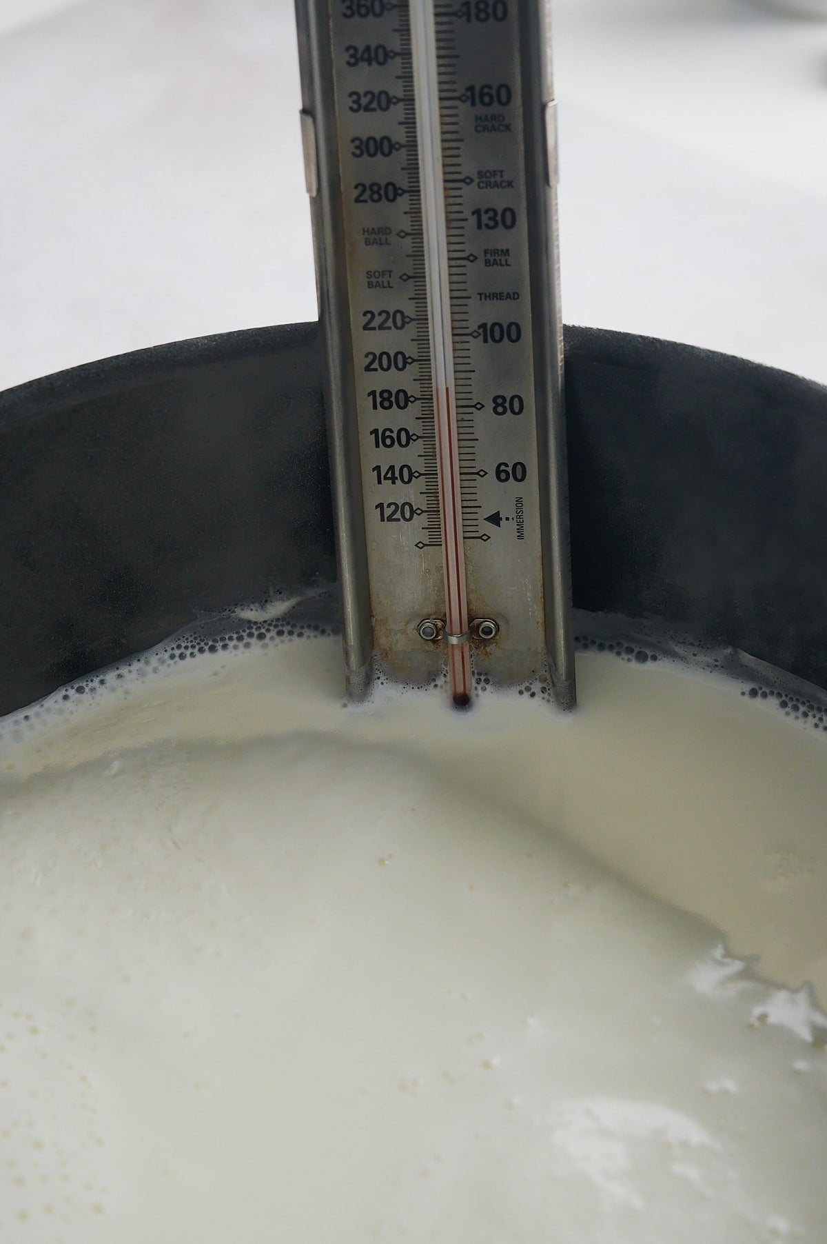 thermometer attached to side of pan reaching temperature for homemade ricotta cheese.