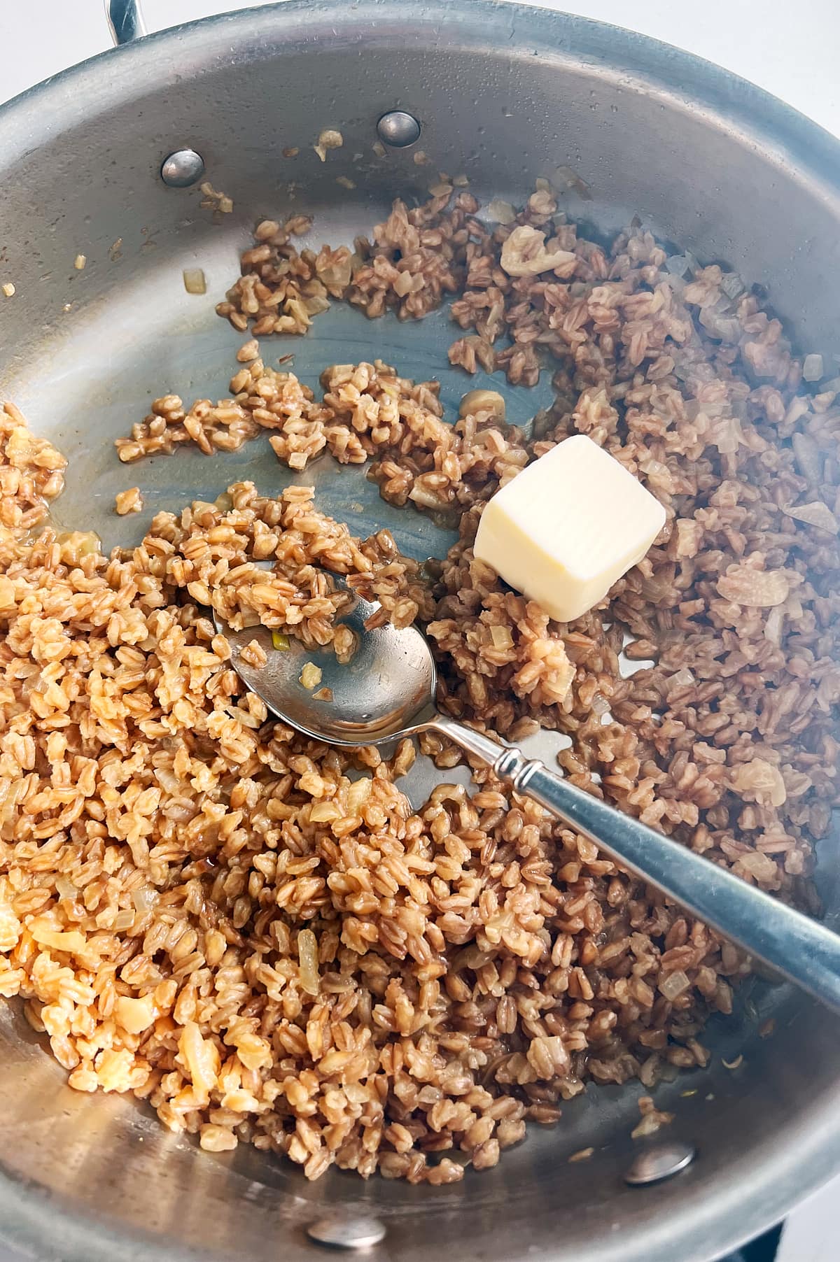 butter being added to skillet of farro risotto.