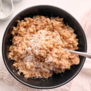 Black bowl with farrotto farro risotto on a cream napkin with salt and pepper.