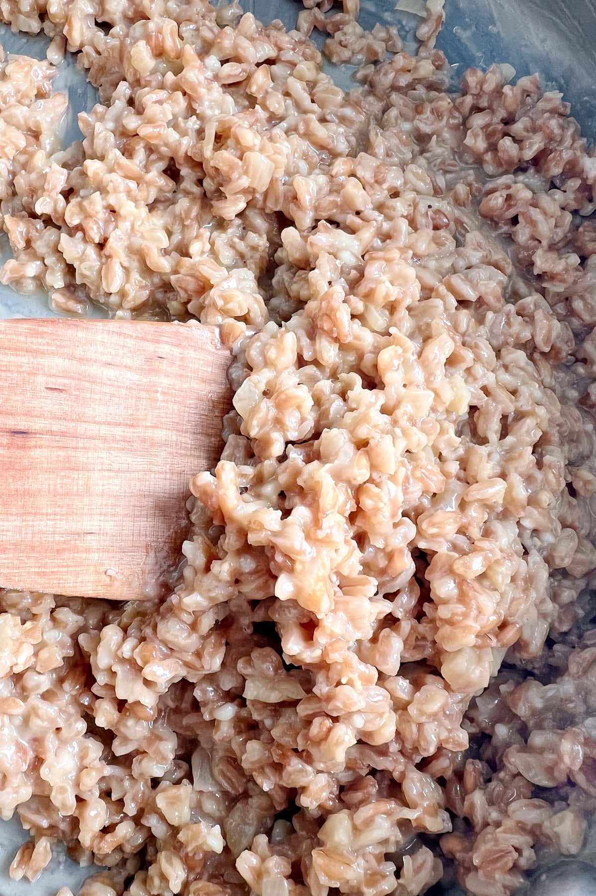 close up of creamy parmesan farrotto being stirred by wooden paddle.