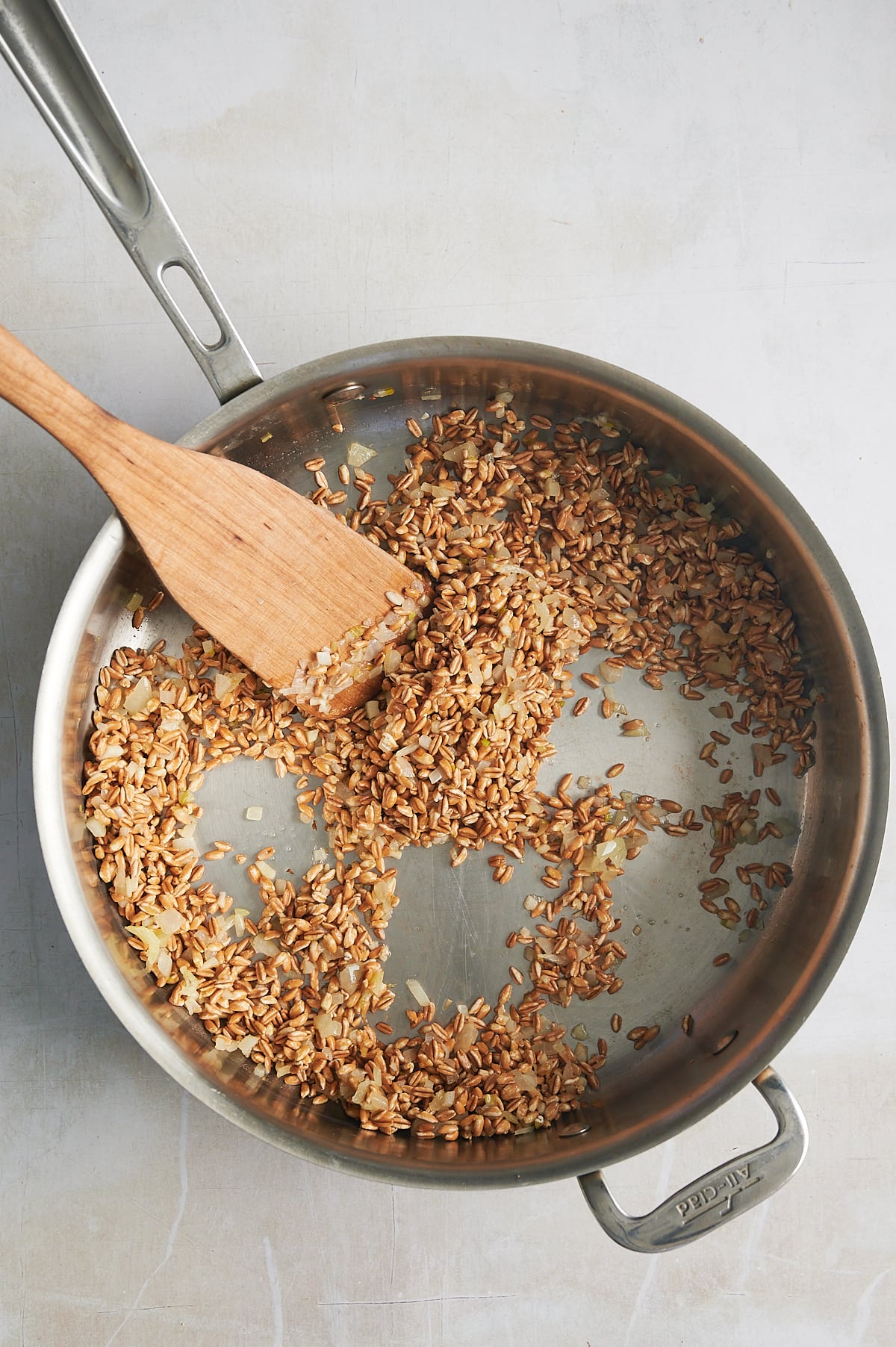 wooden spoon toasting farro in stainless skillet
