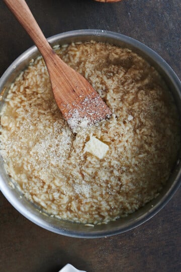 Pat of butter and parmesan being stirred into pan of cooked risotto
