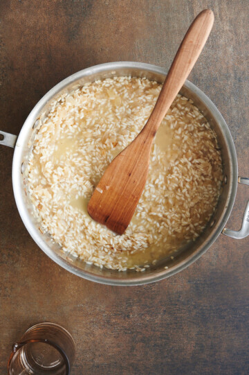 Stainless skillet of risotto halfway cooked with wooden paddle