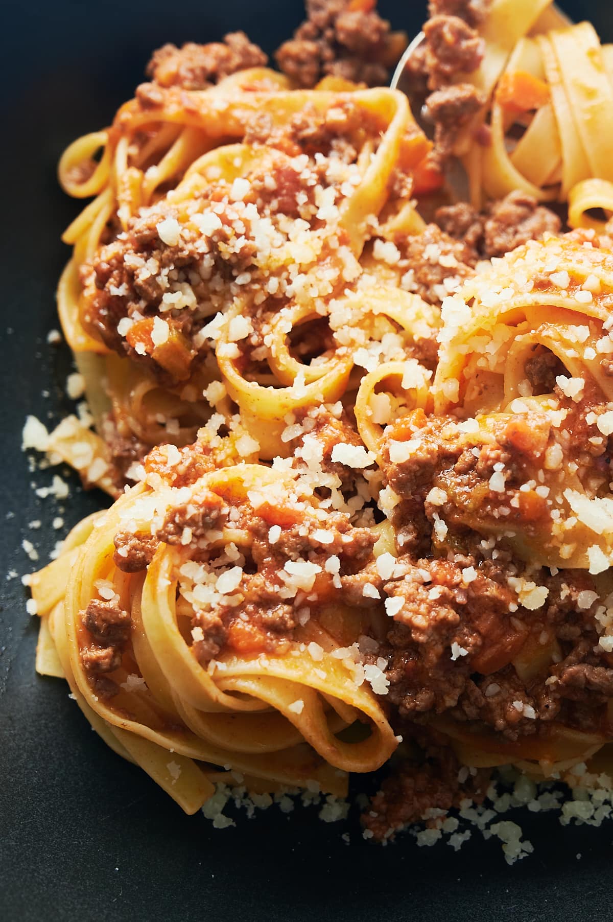 Close up of tagliatelle bolognese with parmesan cheese on a black bowl.