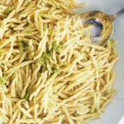 close up of silver spoon stirring bowl of pesto and trofie pasta in a white bowl