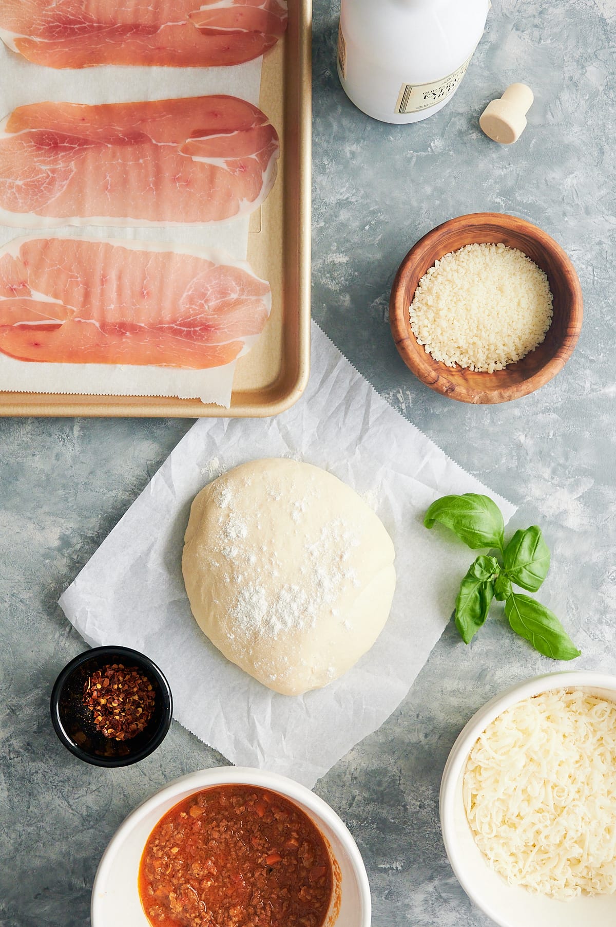 Ingredients for Bolognese Pizza including prosciutto, Bolognese sauce, pizza dough, mozzarella and parmesan.