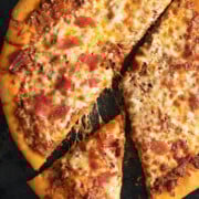 Sliced Bolognese Pizza with cheese pulls on a black pizza stone.