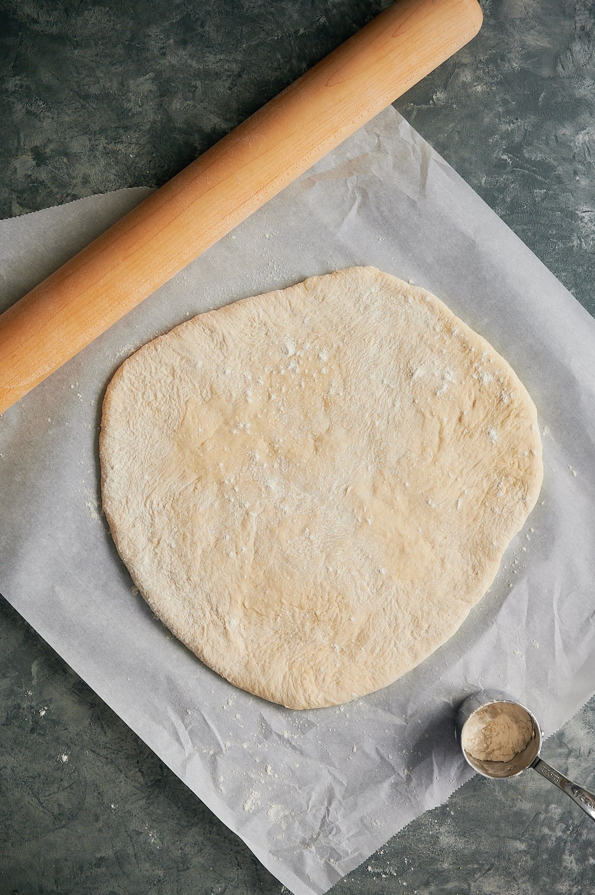 parchment paper with pizza dough rolled up with rolling pin