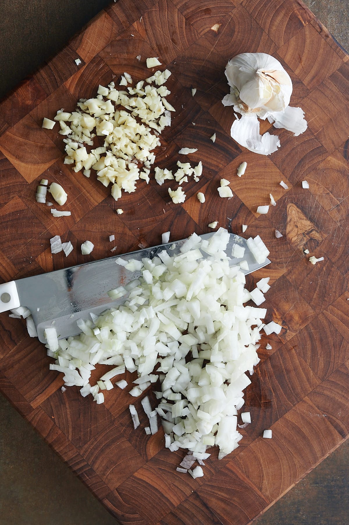 wooden cutting board with diced onion and minced garlic and a knife.