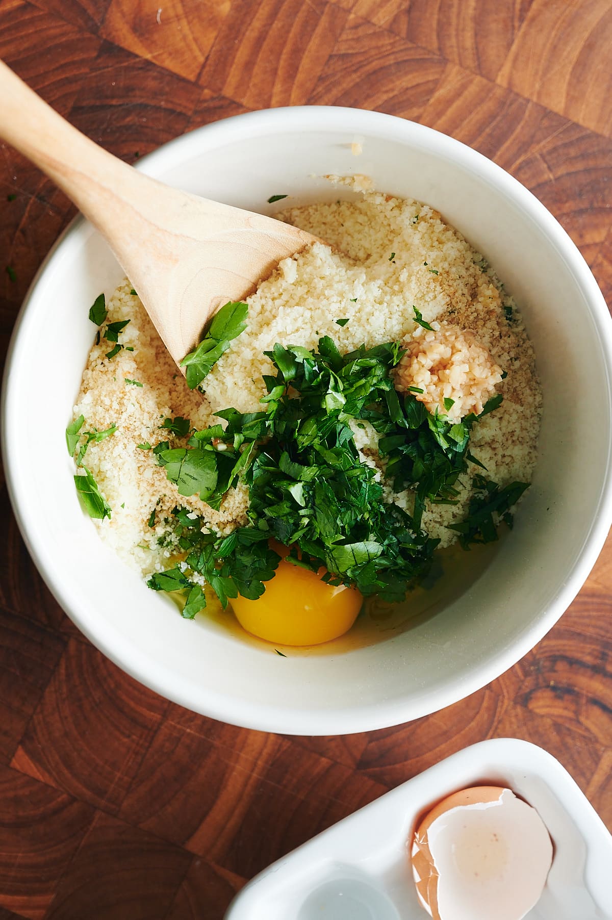 white bowl of ingredients for braciole breadcrumb filling being stirred by wooden spoon.