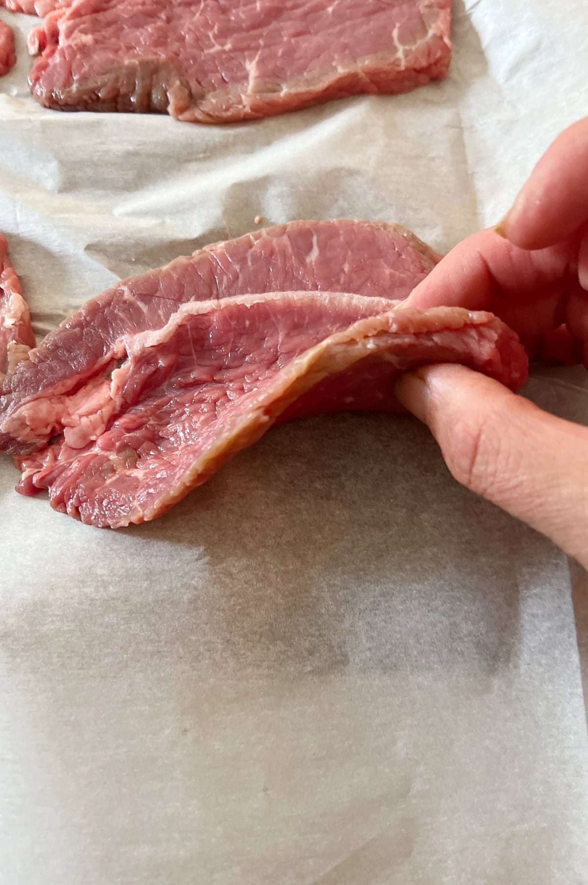 Hand holding thickness of beef round for braciole.