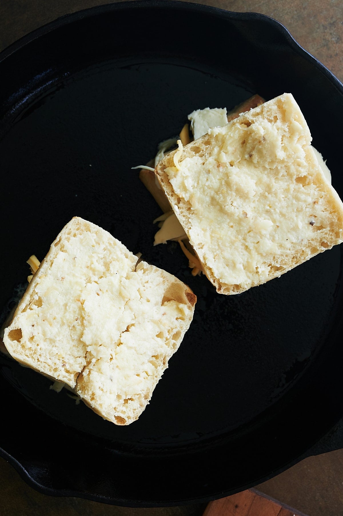 Uncooked tops of garlic bread grilled cheese sandwiches in cast iron skillet.