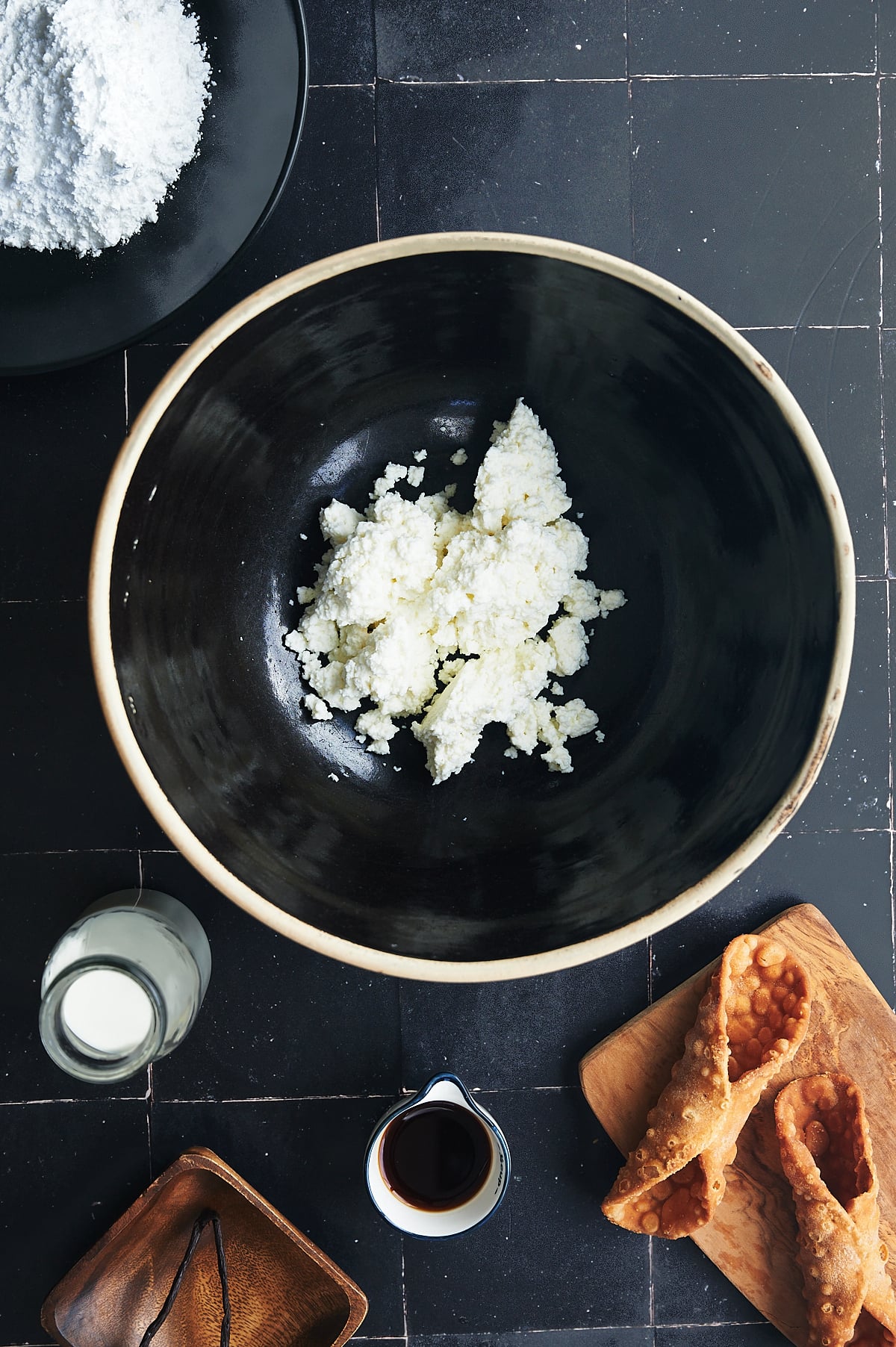 black bowl of ricotta cheese surrounded by ingredients to make cannoli dip