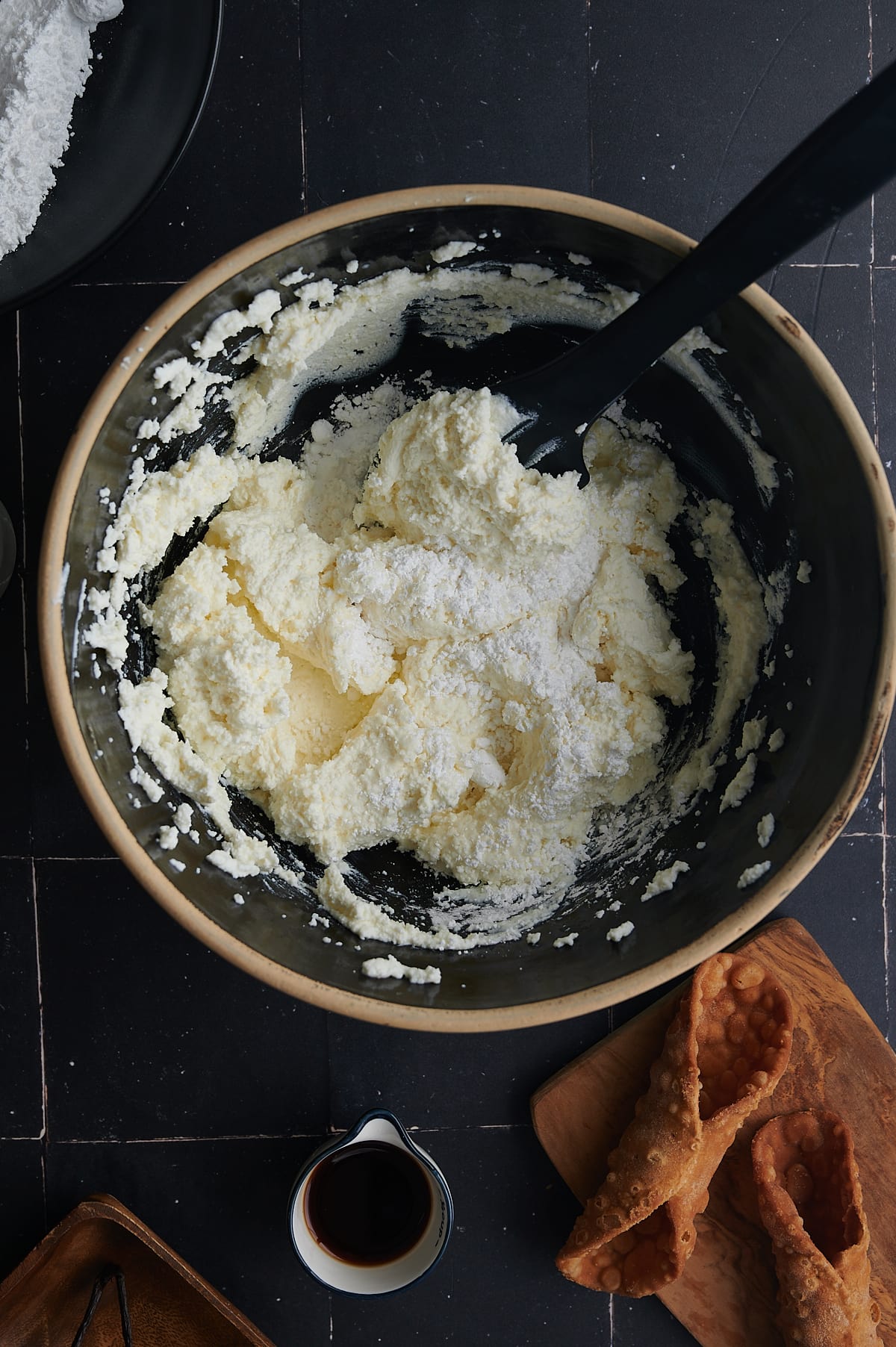 cannoli filling being mixed with powdered sugar in black bowl.