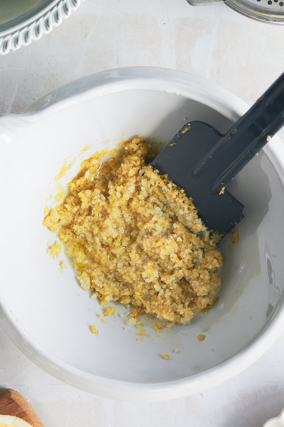 black spatula mixing lemon pesto in white bowl.