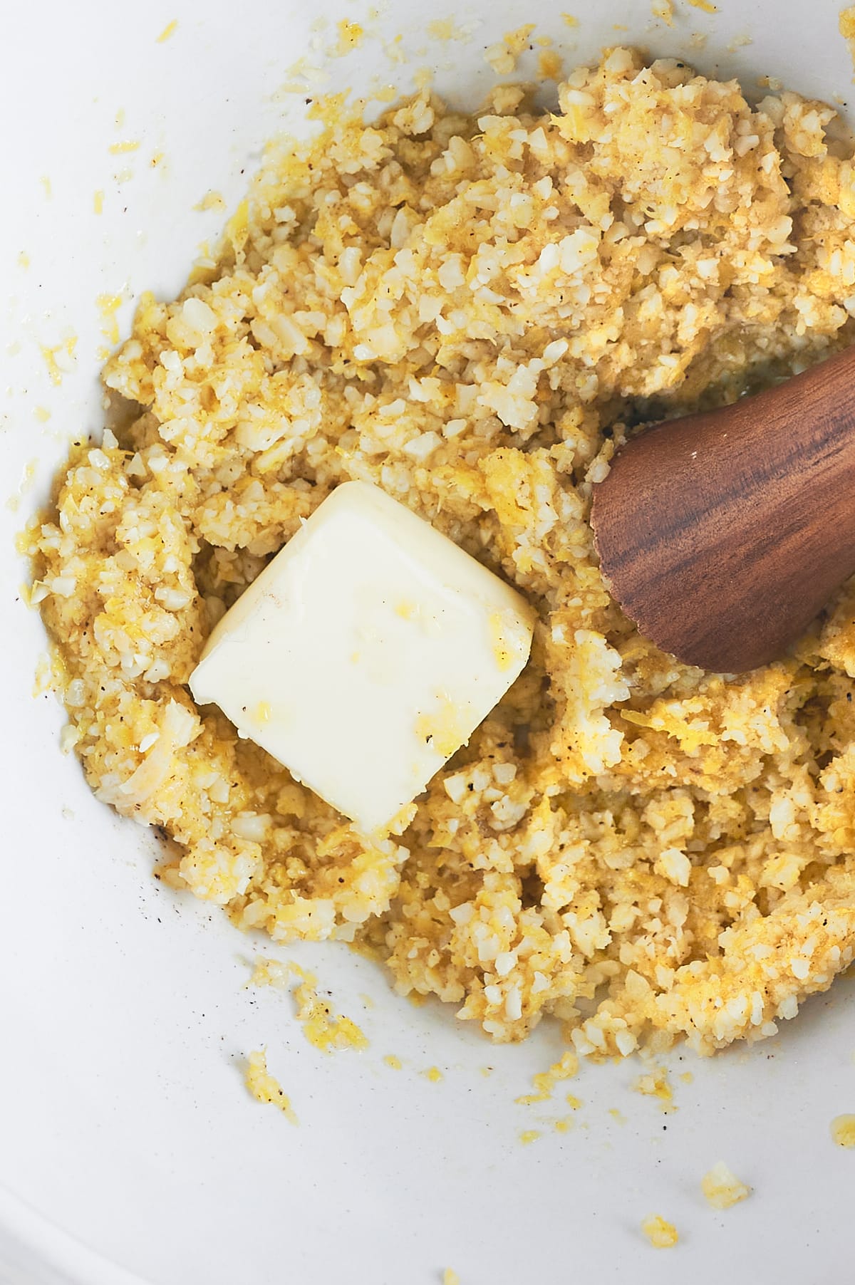 butter being muddled into lemon pesto in white bowl.