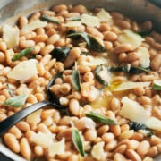 close up of cannellini beans with fresh sage leaves and parmesan.