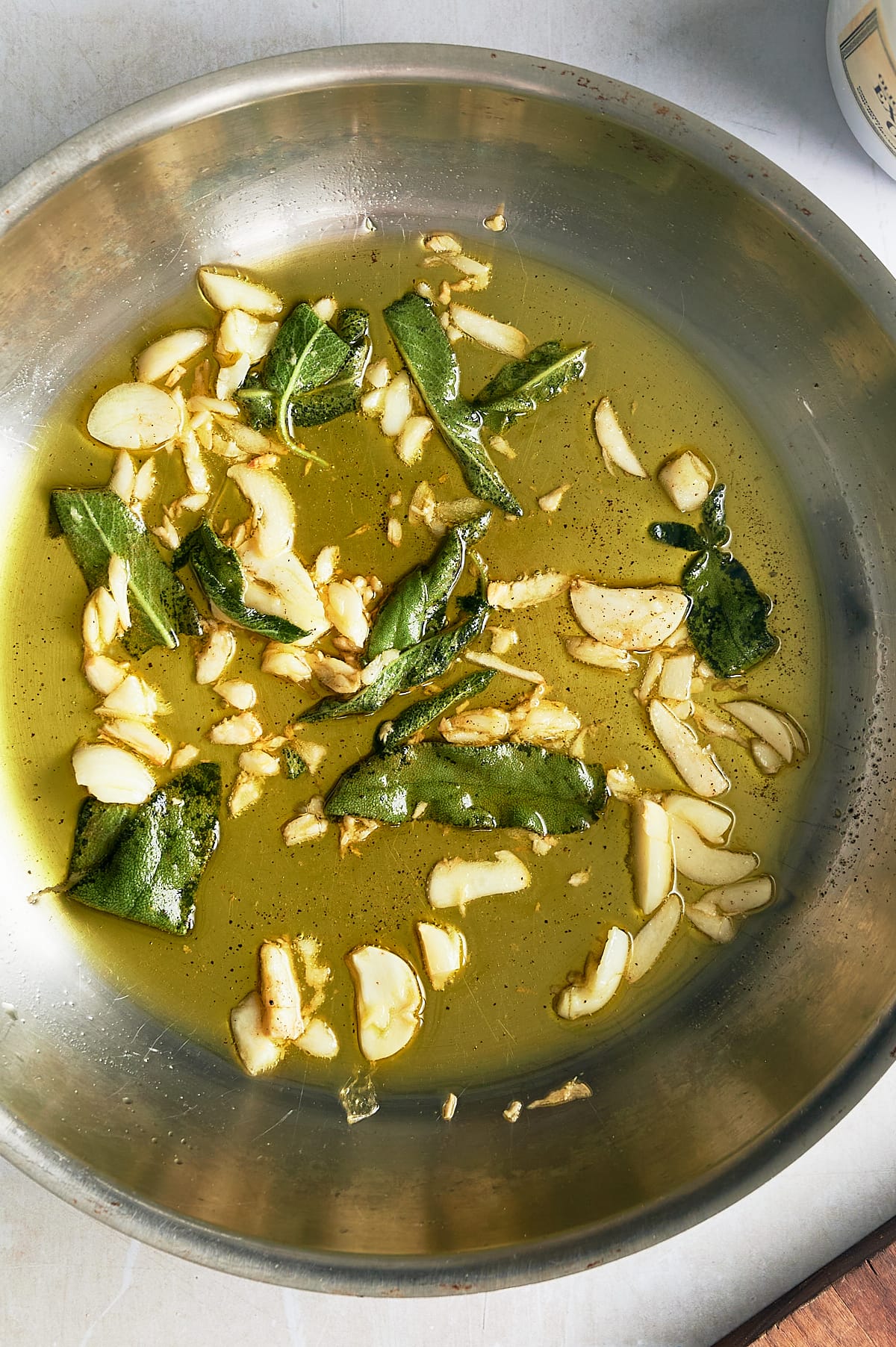 stainless skillet of sliced garlic and sage leaves simmering in olive oil.