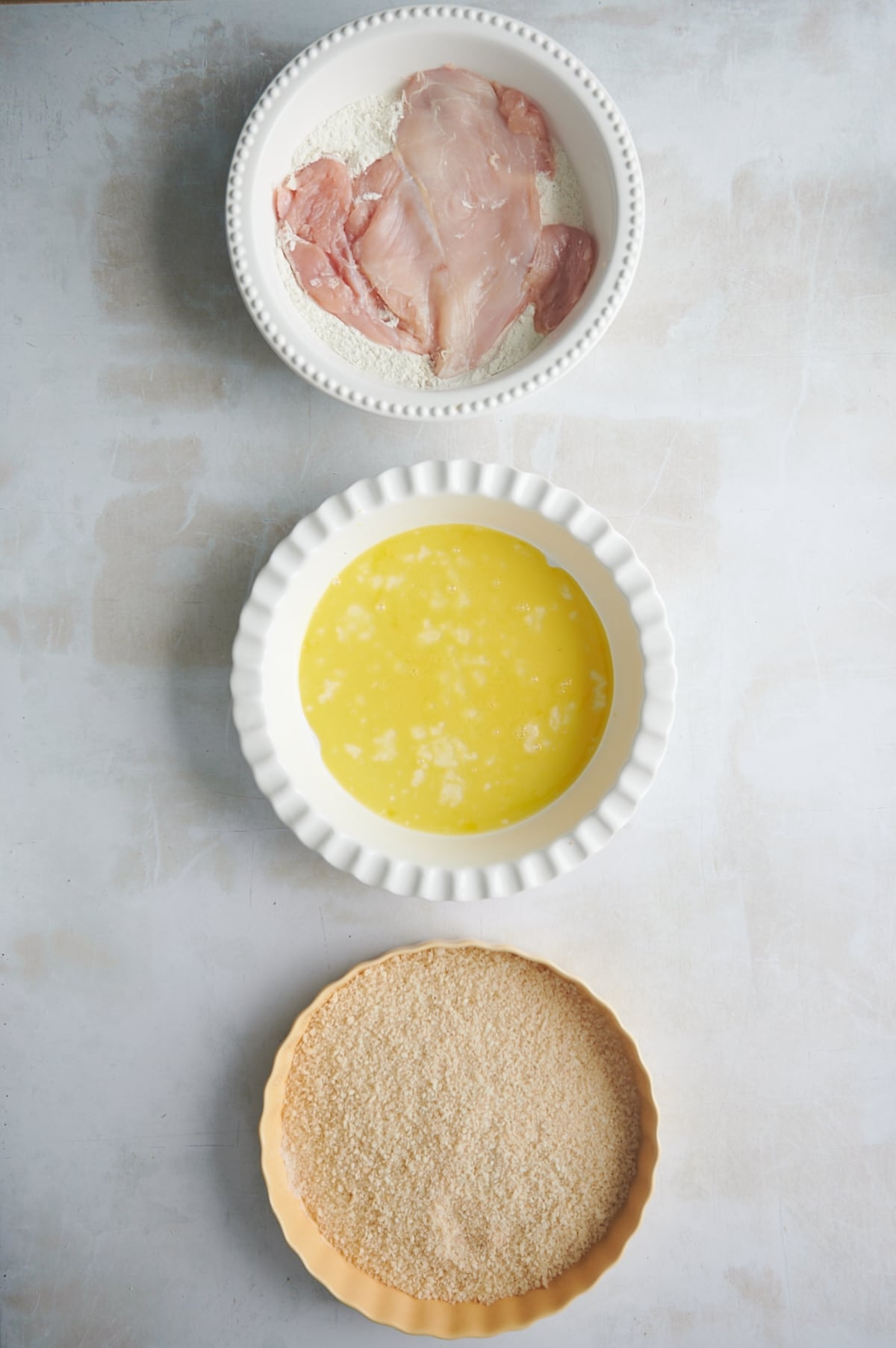 White pie plate with chicken in flour for step 1 of breading process