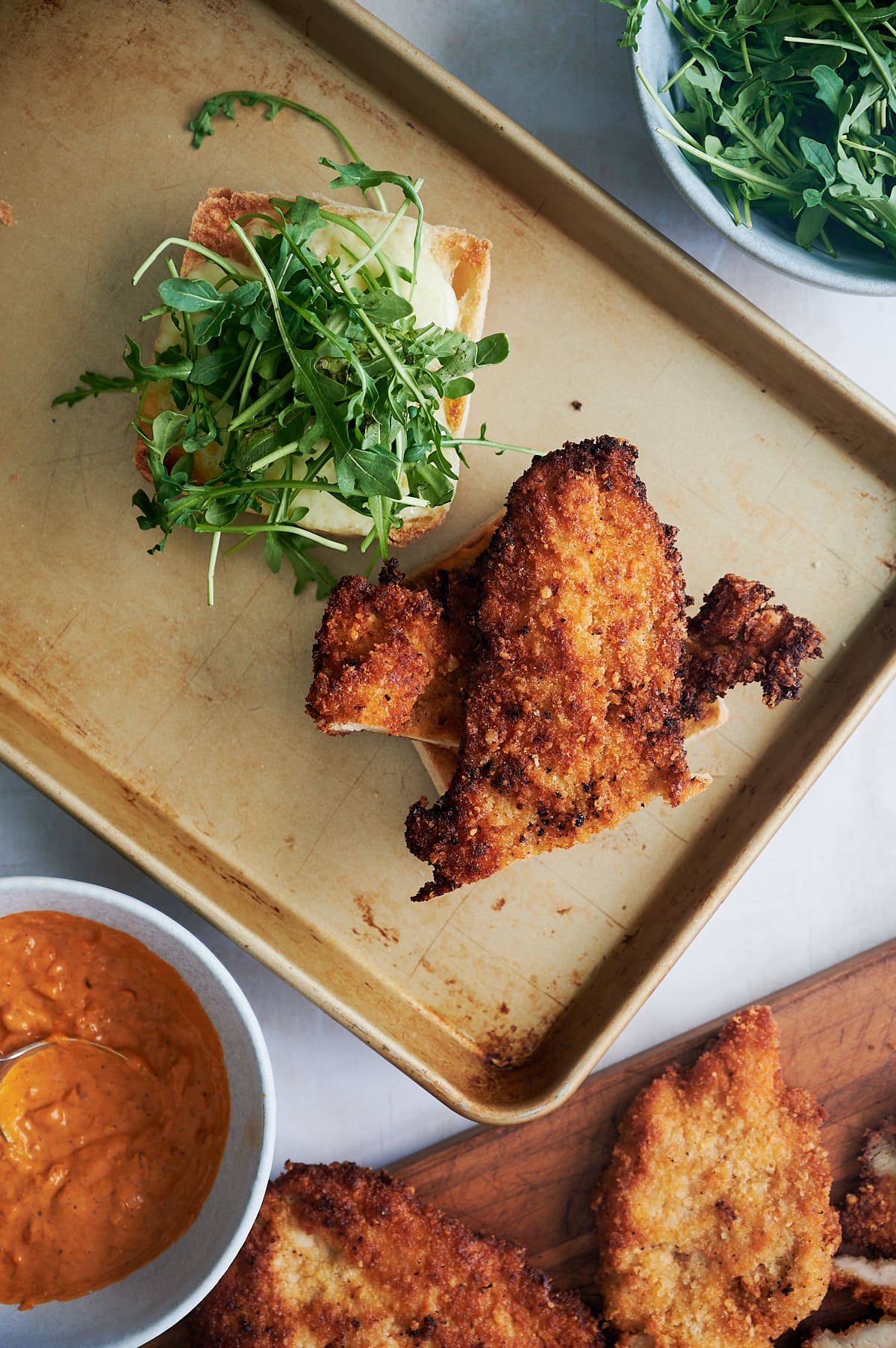 Chicken cutlets on open faced roll with arugula on a sheet pan.