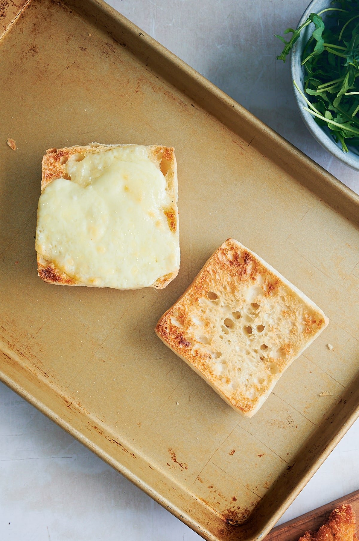 sheet pan with toasted ciabatta rolls topped with melted cheese.