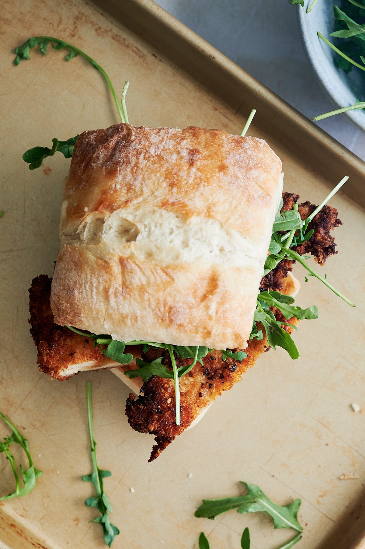 Top of a chicken cutlet sandwich on a sheet pan with arugula.