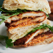 front view of white plate with chicken cutlet sandwich stacked with a skewer through the top.