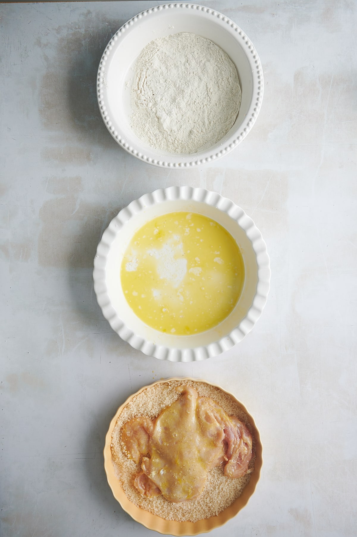 chicken dipped in egg being dipped in breading for cutlets.