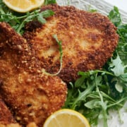 White platter of fried chicken cutlets on arugula
