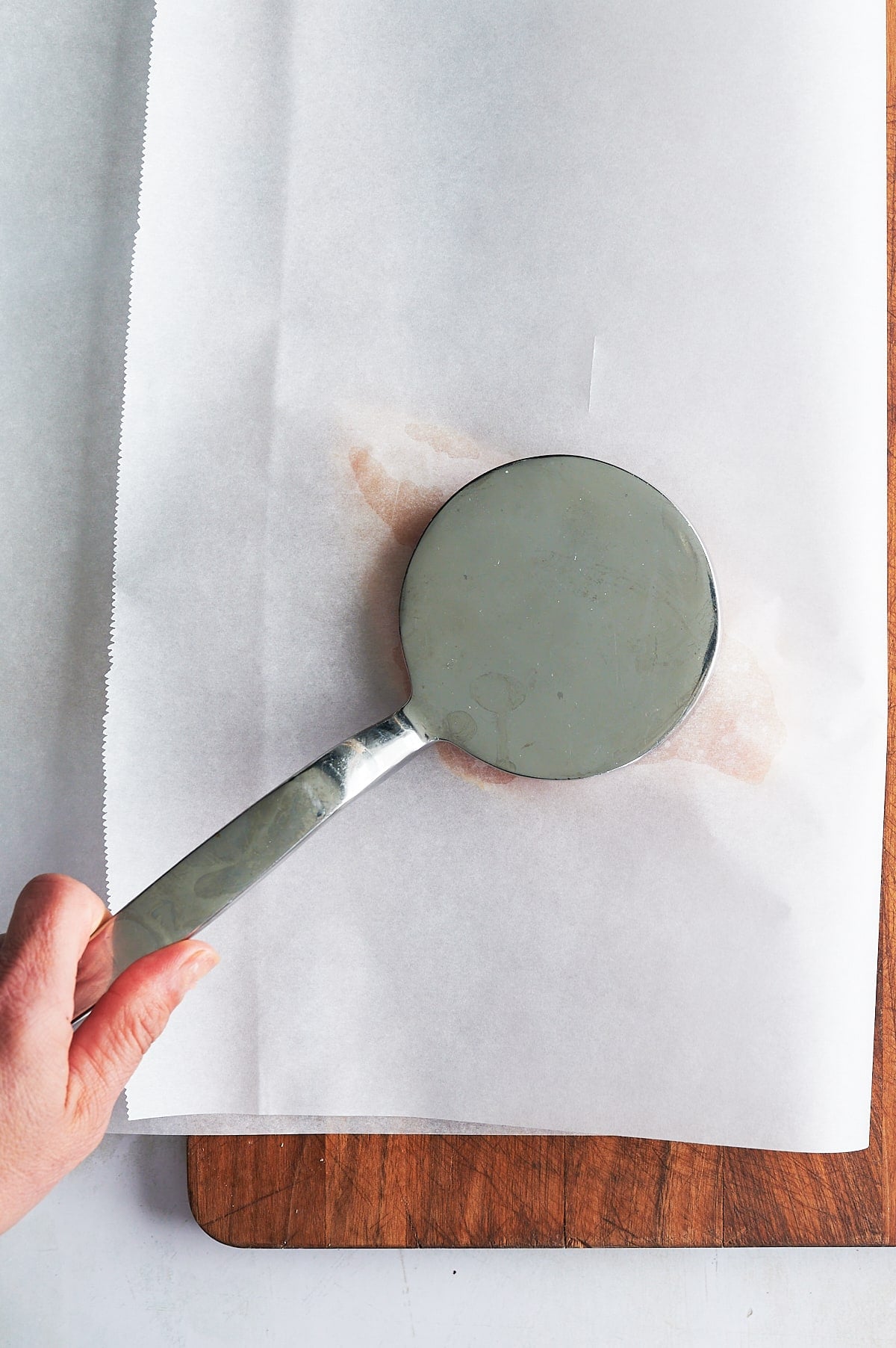 Parchment paper over chicken breasts being pounded flat with mallet.
