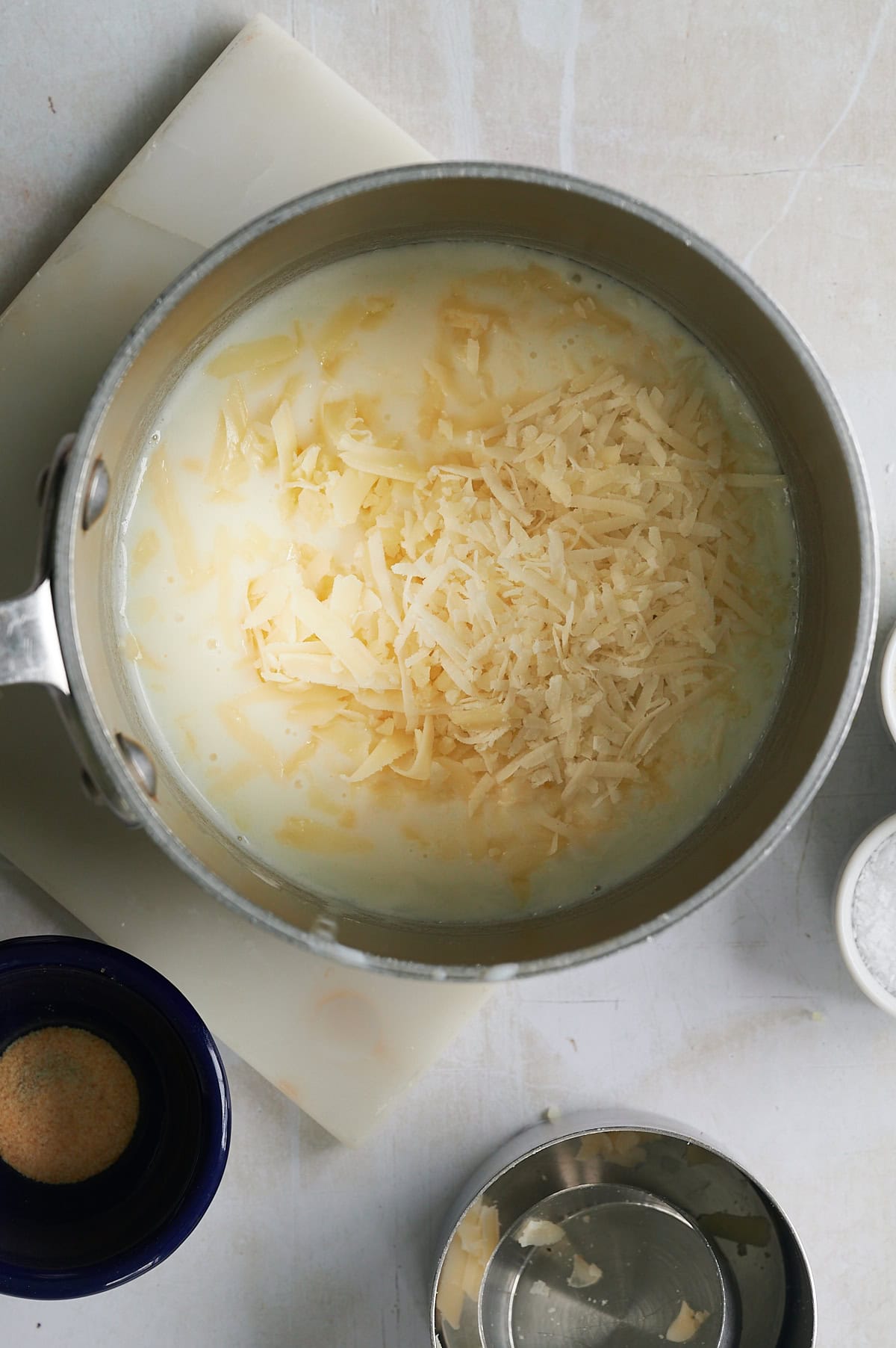 Adding grated cheese to white sauce in a saucepan.