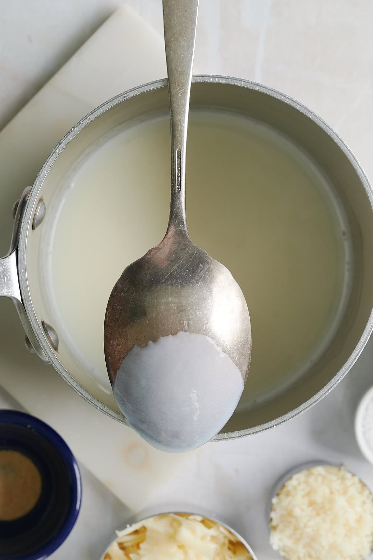 Saucepan with white sauce topped with sauce coating back of spoon.
