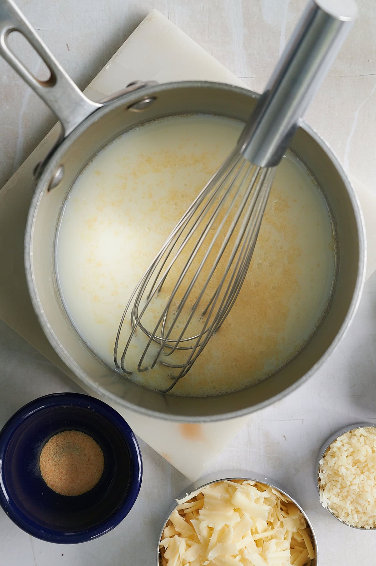 Saucepan with milk being added to cheese sauce.