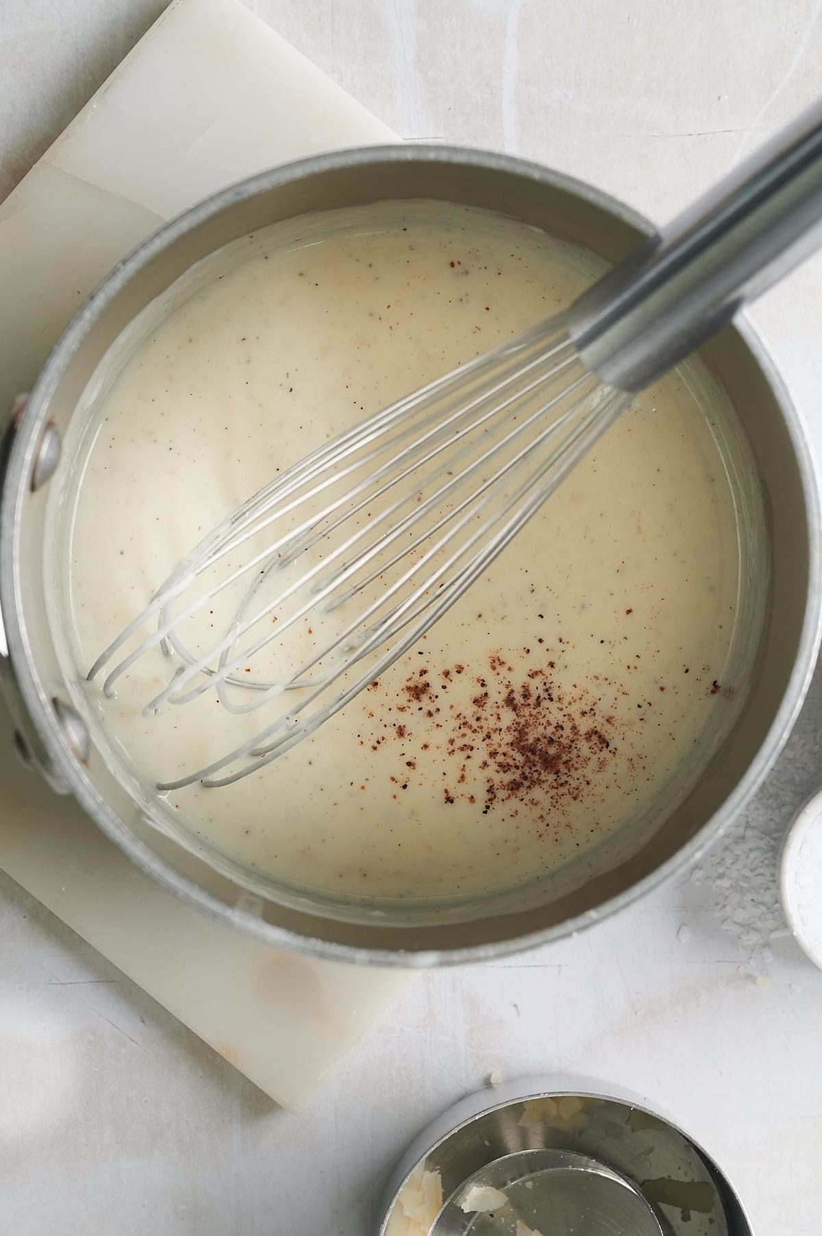 Nutmeg being whisked into cheese sauce in pan.