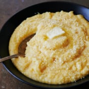Silver spoon in black bowl of finished polenta with butter and parmesan cheese.