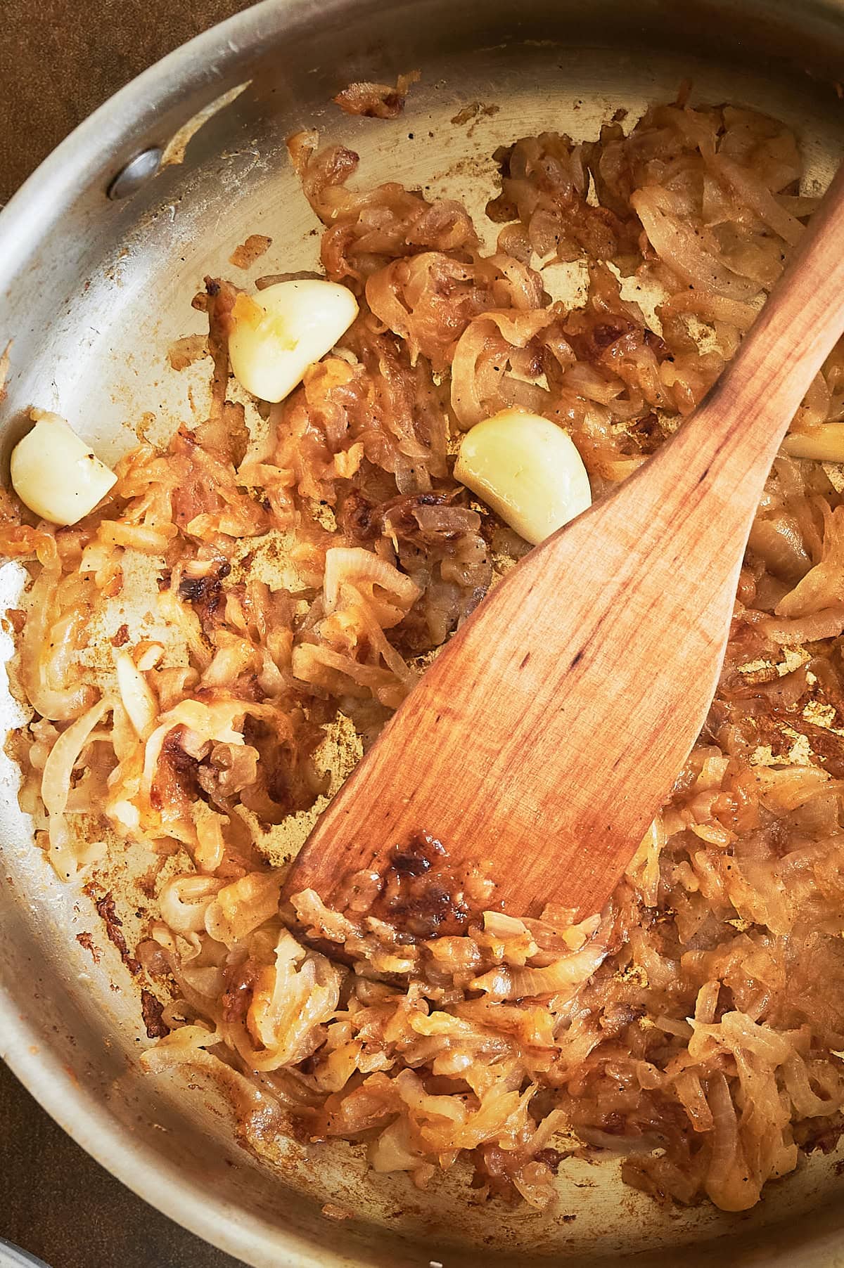 garlic cloves in caramelized onions being stirred in pan.
