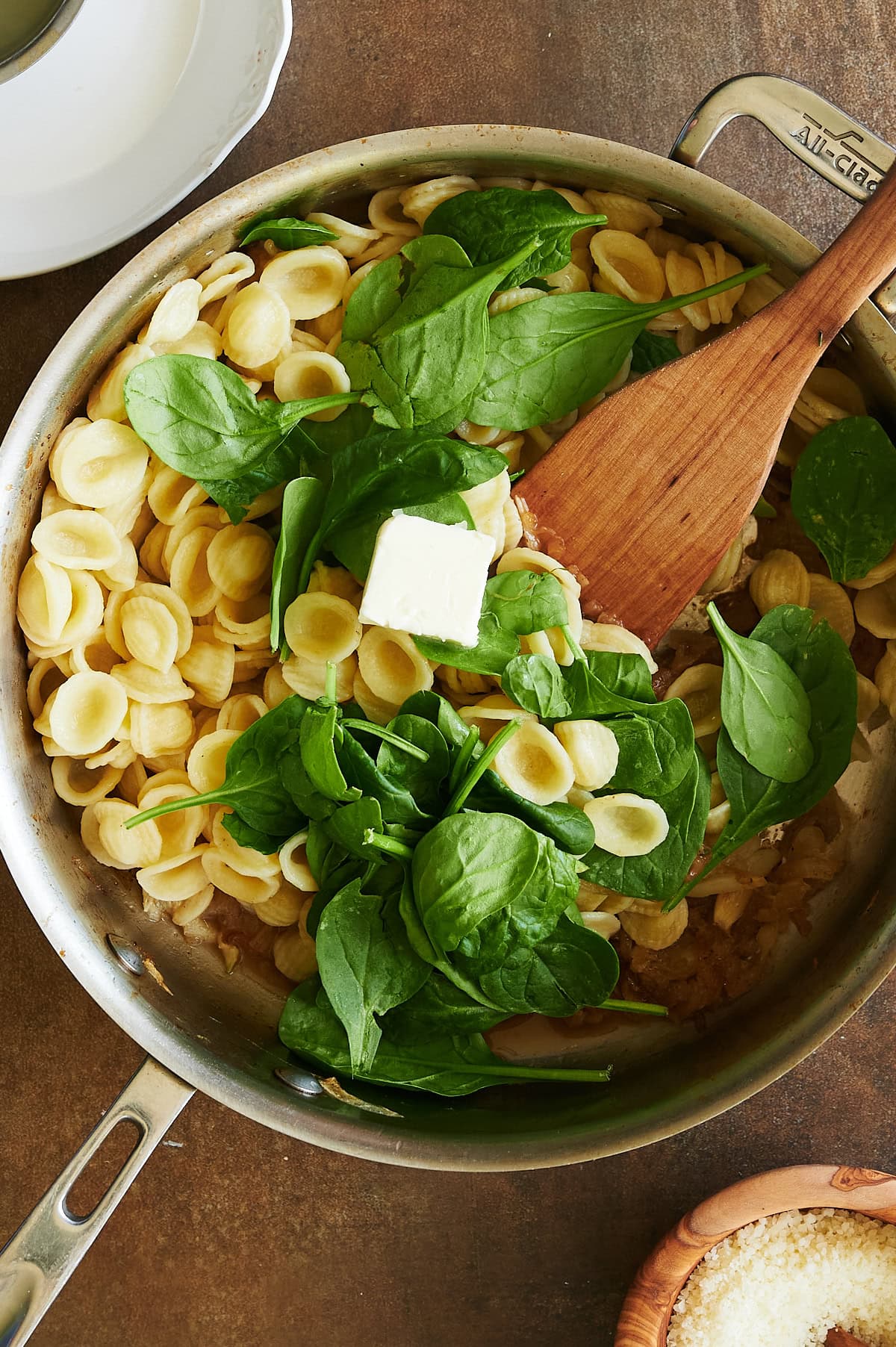 pat of butter being stirred into orecchiette pasta with spinach.