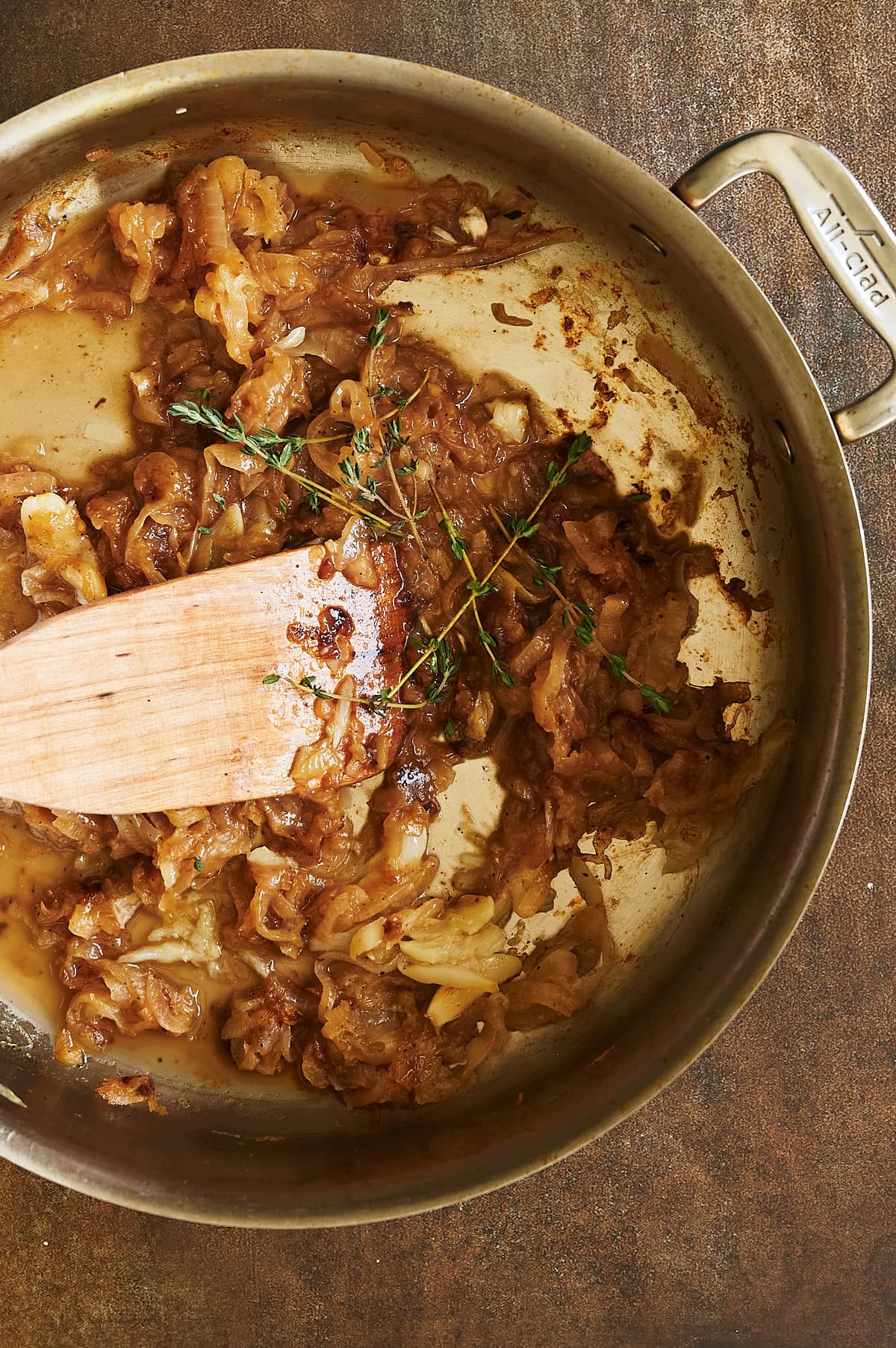 stainless pan of caramelized onions being stirred with paddle and sprigs of fresh thyme.