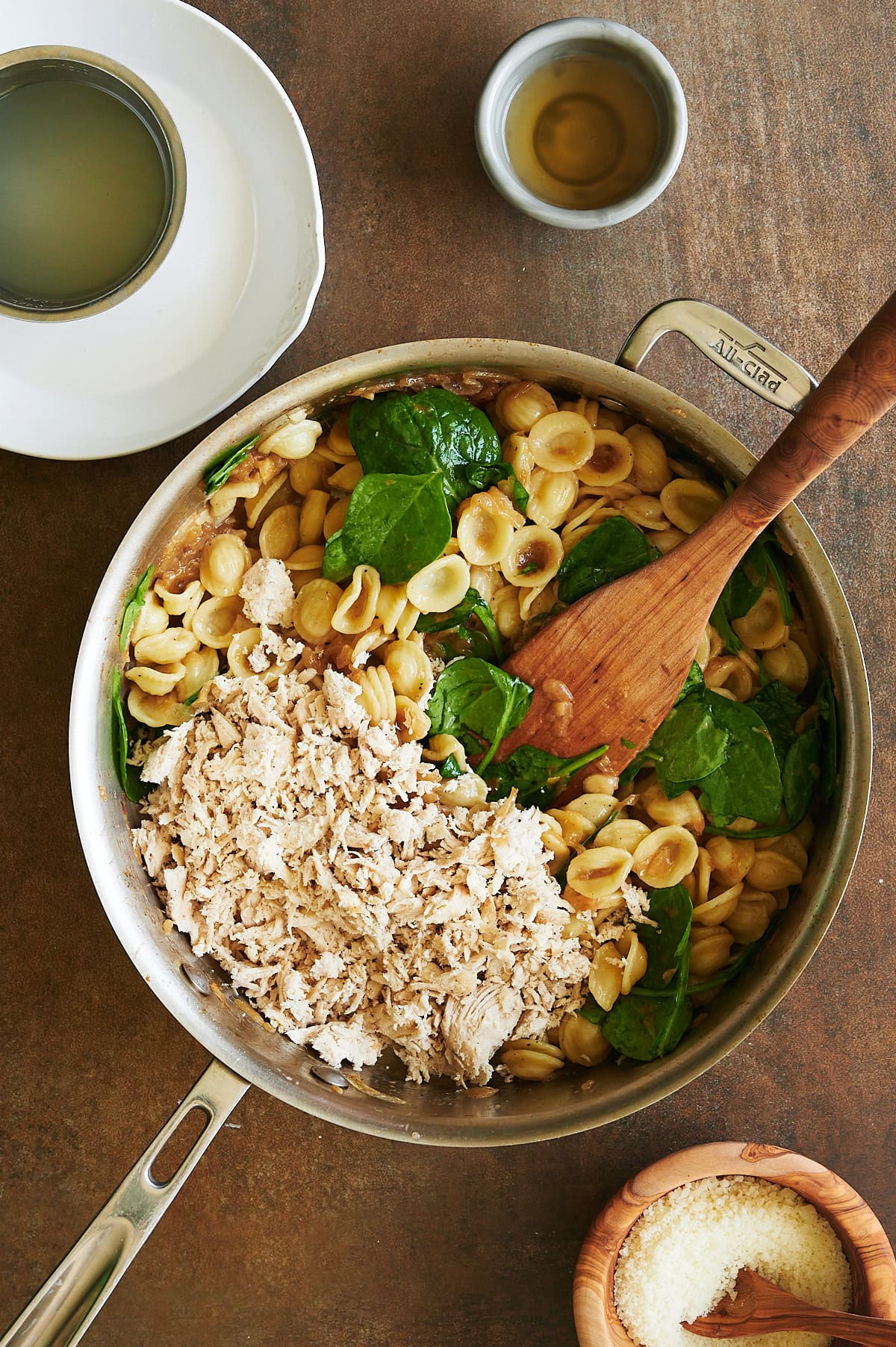 stainless pan with wooden paddle stirring chicken into orecchiette pasta with spinach