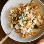 white bowl with orecchiette pasta tossed with chicken, spinach and caramelized onions.