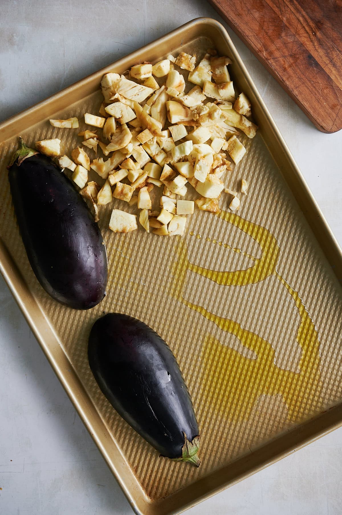 Sheet pan drizzled with olive oil with 2 eggplant halves and diced eggplant.