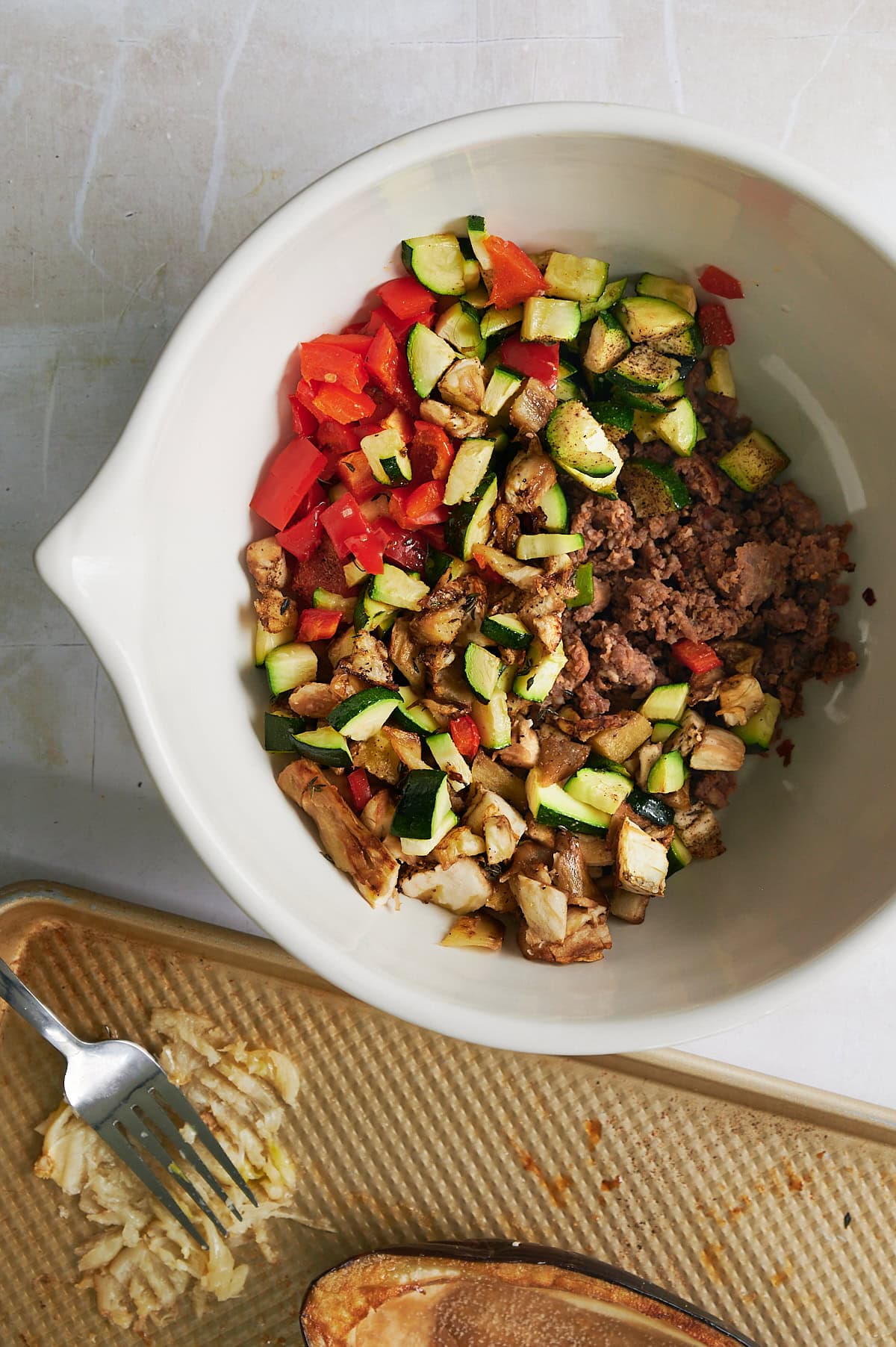 Cooked stuffed eggplant filling with smashed garlic cloves on sheet pan.